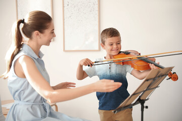 Young woman teaching little boy to play violin indoors © New Africa