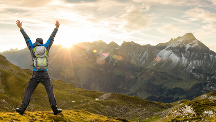 Successful Hiker Man with Backpack jumping with raised arms. Amazing sunrise in the mountains with...