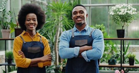 Portrait of happy man and woman in aprons standing at own small flower shop and smiling to camera after reopening African American joyful couple entrepreneurs running own floral business Store concept