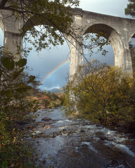 Fototapeta na wymiar Autumn view of a mountain stream flowing under a big stone viaduct and rainbow after rain. Glenfinnan Viaduct, Scotland, United Kingdom