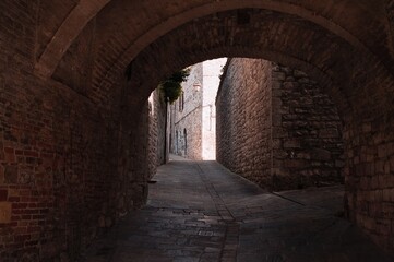 Fototapeta na wymiar The view of an ancient alley under an architectural arch in a medieval Italian village (Gubbio, Umbria, Italy)