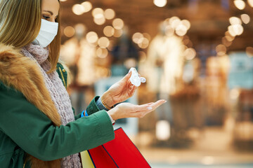 Midsection of adult woman in mall wearing a mask and using hand sanitizer