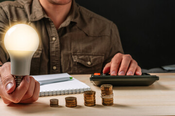 Business man hand holding a light bulb using a calculator to calculate cash flow. The idea of...