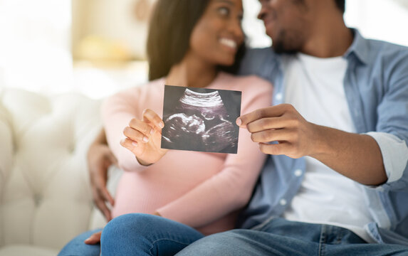 Positive black couple showing ultrasound photo of their unborn baby at home, selective focus on hands