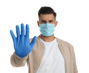 Man in protective face mask and medical gloves showing stop gesture against white background, focus on hand