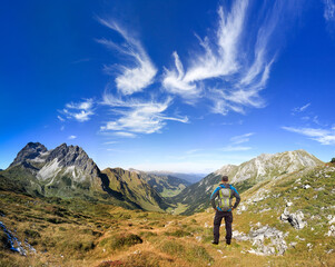 Fototapeta premium Hiker Man with Backpack enjoying great clear view in the mountain with beautiful clouds. Alps, Kleinwalsertal, Gemsteltal, Austria.