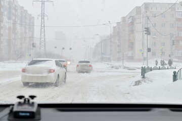 Snowfall and the wind in the city in winter. Snow covered road and cars and frozen people.