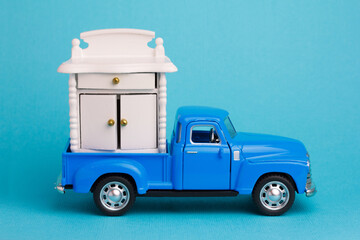 Blue toy pickup truck transports wardrobe. Furniture delivery service and Moving day concept. - obrazy, fototapety, plakaty