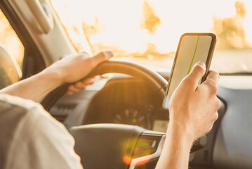 A man sits in a car and looks at his phone with the Navigator app on a Sunny day