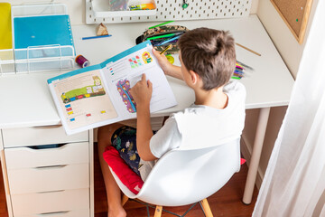 Boy studying and doing homework sitting at his desk in his bedroom at home
