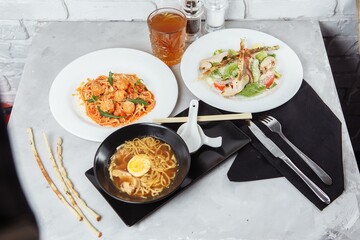 three-course set on a table in a restaurant, cafe menu. Business lunch from bowl ramen with chicken and egg, fresh caesar salad and pasta