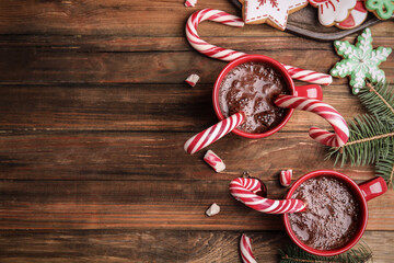 Flat lay composition with cups of hot chocolate and Christmas candy canes on wooden table. Space for text