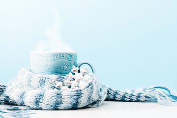 Blue cup with steam. Cup of hot drink in warm scarf on blue background. Front view, copy space