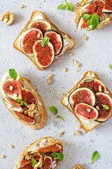 Crispy bruschetta with soft ricotta, ripe figs, walnuts and pine nuts, mint and honey on a light background. Figs fruit toast on marble table with honey and walnut. Top View.