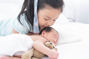 little sister hugging her newborn brother. toddler kid meeting new sibling. love, trust and tenderness. cute girl and new born baby boy relax in a white bedroom. family with children at home.