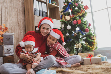 parent and two little children having fun and playing together near christmas tree indoors. merry christmas and happy holidays. cheerful mom and her cute daughters girls exchanging gifts.