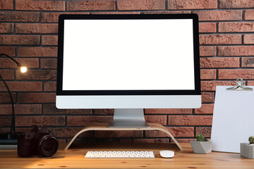Fototapeta premium Comfortable workplace with modern computer on wooden table near brick wall. Space for text