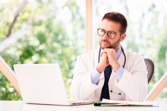 Portrait shot of male doctor working on notebook while sitting at desk in doctor's office.