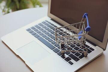 Internet shopping. Laptop with small cart on table indoors, closeup