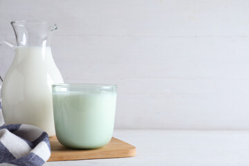 Jug and glass with fresh milk on white wooden table. Space for text