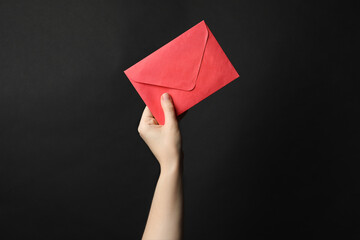 Woman holding red paper envelope on black background, closeup