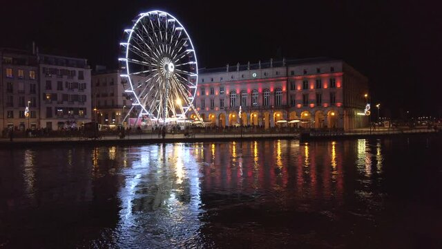 Static shot of the ferris wheel and the town hall at night, with their reflection on the Nive river, Bayonne, France.