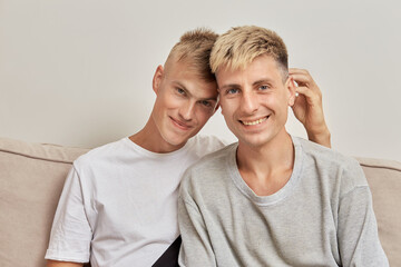 Portrait of two beautiful blond guys sitting at home on the sofa. They look into the camera.