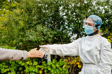 A patient stretches out his hand to a doctor during the coronavirus pandemic. A doctor in a protective suit gives a hand to the patient. Social distance between doctor and patient during Covid-19