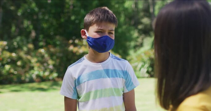 Portrait of caucasian brother and sister wearing face mask standing in the garden