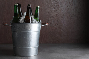 Metal bucket with bottles of beer and ice cubes on grey table, space for text