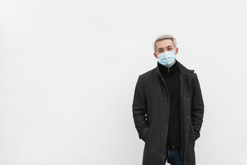 A man in a medical mask on a white background on the street looks at the camera