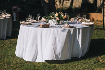 A large round table with a white tablecloth and dishes, a bouquet of flowers stands on the green...