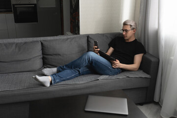 A man working at home on the couch with a tablet and a phone in his hands