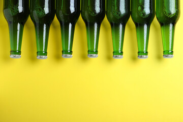 Bottles of beer on yellow background, flat lay. Space for text