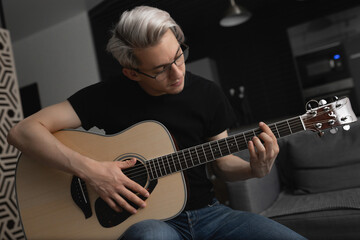 Man with white hair wearing glasses playing guitar at home