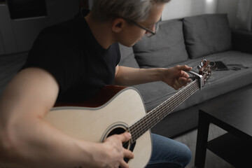 Man with white hair wearing glasses playing guitar at home