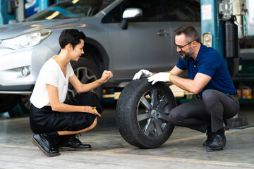 Expertise mechanic man showing the tread of a old tire to a female customer at Car maintenance and auto service garage