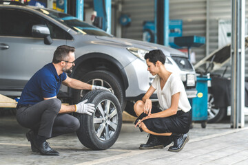 Expertise mechanic man showing the tread of a old tire to a female customer at Car maintenance and auto service garage