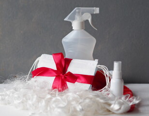 Pack of medical masks, Santa Claus hat and antiseptic on a gray background. Idea of celebrating Christmas during the coronavirus pandemic, be sure to use your virus protection during the holiday
