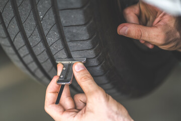 Mechanic checking checking the depth of car tire tread.  Car maintenance and auto service garage concept.