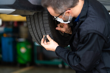 Mechanic checking checking the depth of car tire tread.  Car maintenance and auto service garage concept.