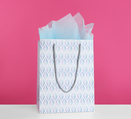 Gift bag with paper on white table against pink background