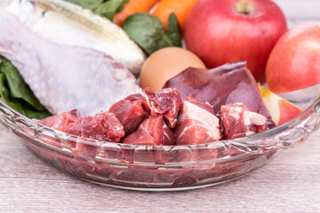 Close-up on ingredients of barf raw food recipe for dogs consisting meat, organs, fish, eggs and vegetable