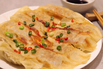 Fried dumplings gyoza with crispy skin served with green onion, red peppers and soy dipping sauce. Chopsticks are utensils for dim-sum.