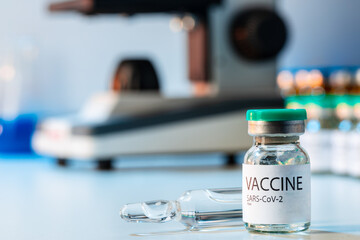 Vial of Covid-19 vaccine next to a microscope