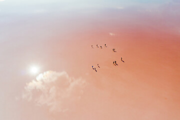 Cartoon figures of people on a pale pink background of a salt lake. The lake reflects the sun and clouds. Shooting from the air.