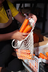 Close-up of female hands put raw carrots in an eco bag. Eco goods replacement of a plastic bag. Fresh vegetable on the market.