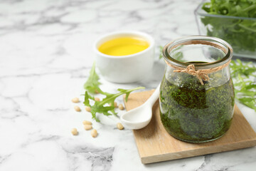 Jar of tasty arugula pesto and ingredients on white marble table
