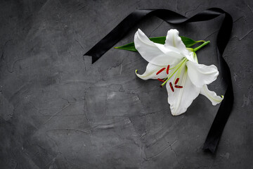Flat lay of lily flowers and black ribbon. Funeral symbol - obrazy, fototapety, plakaty