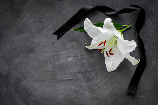 Flat lay of lily flowers and black ribbon. Funeral symbol